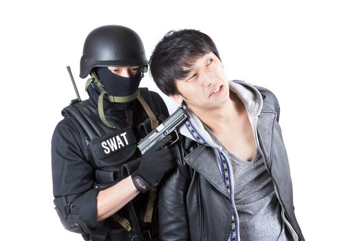 SWAT装備の隊員に拘束されるグレーの服の男性