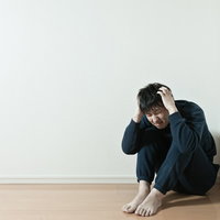 膝を抱えて頭を抱える黒い服の男性の写真