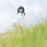 草の丘の上で右腕を上げるツインテールの女性の後ろ姿の写真