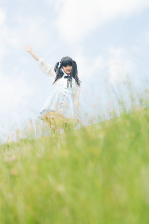 草の丘の上で右腕を上げるツインテールの女性の後ろ姿