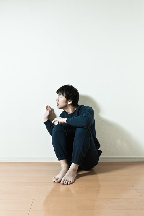 壁際で膝を抱えて横を向く男性