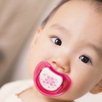おしゃぶりを咥えてこちらを見る赤ちゃんの写真