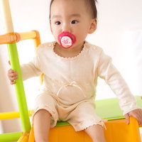 おしゃぶりを咥えて遊具に座る赤ちゃんの写真