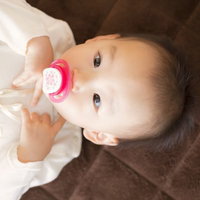 おしゃぶりと哺乳瓶を持つ赤ちゃんの写真