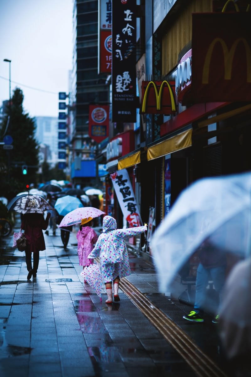 雨の商店街でカラフルな傘とカッパを持つこども