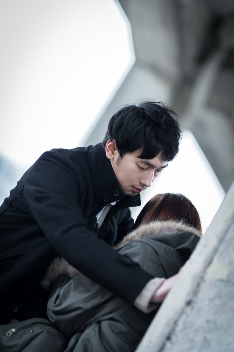 白い壁の前で男性に身を寄せられキスするカップル［モデル：大川竜弥］