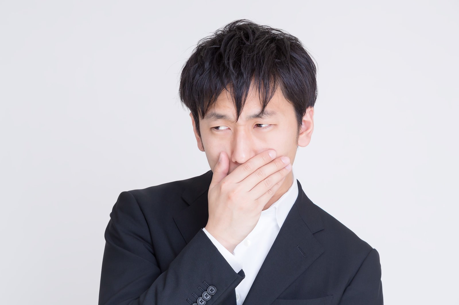 口に手を当てて横目を向くスーツ姿の男性［モデル：大川竜弥］