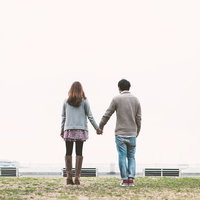 公園で手をつなぐカップルの後ろ姿の写真