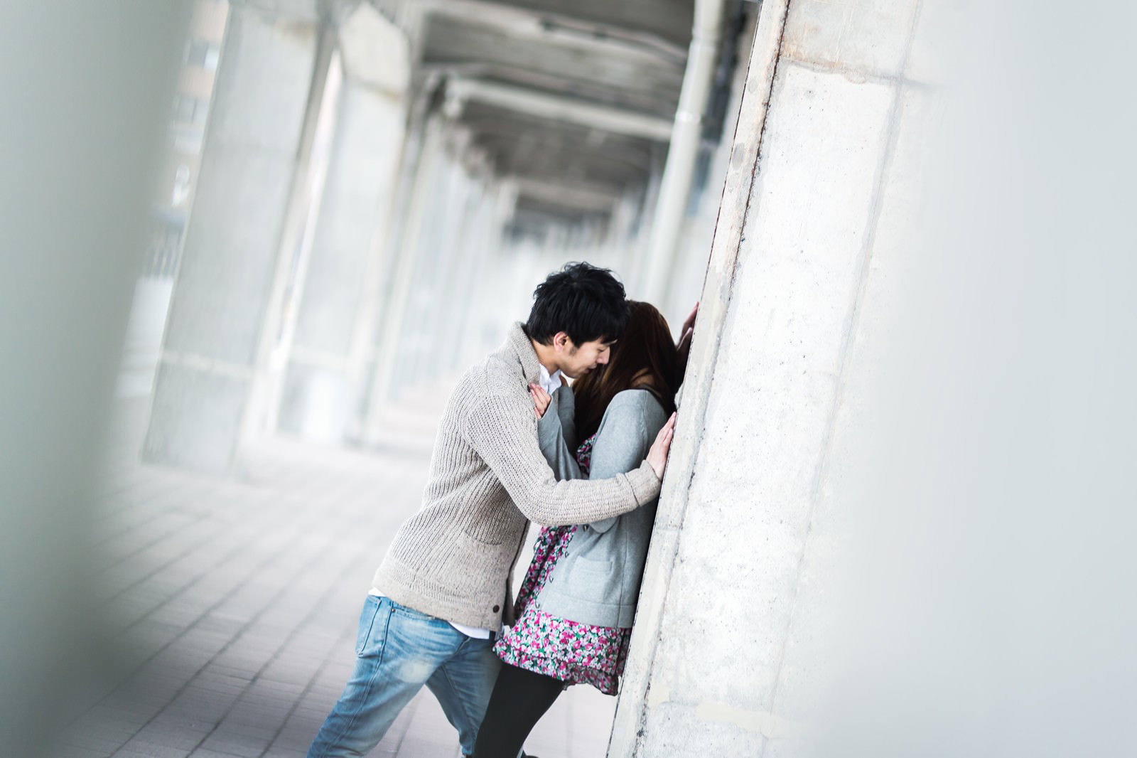 白い柱が並ぶ屋外の通路でカップルが柱に寄りかかって抱き合っている［モデル：大川竜弥］