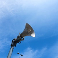 青空を背景に屋外設置のスピーカーのローアングルの写真