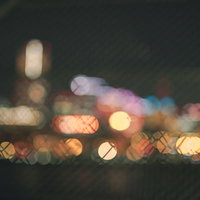 金網越しに見える街明かりの丸ボケ。ネオン光の輝きの写真