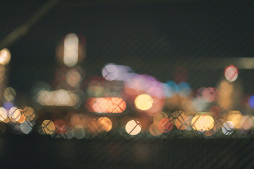 金網越しに見える街明かりの丸ボケ。ネオン光の輝き