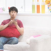 彼女の部屋でソファーに座ってスマホをチェックする男性の写真