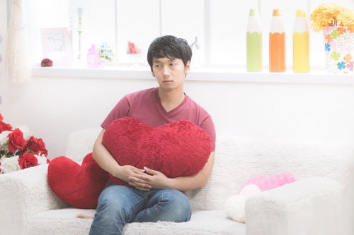 赤いハート型クッションを抱える男性の悩ましい表情