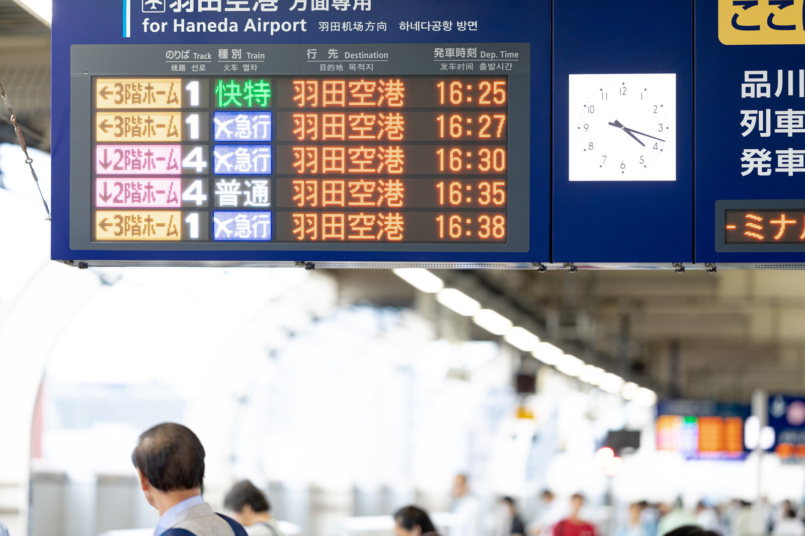 駅のホームにある青い電光掲示板に羽田空港行きの時刻表が表示されている
