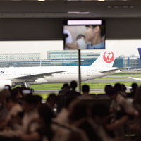 空港の出発ロビーで待つ人々と駐機する旅客機の写真