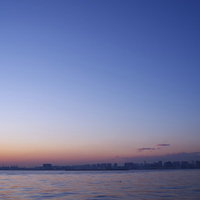 夕焼け空と海沿いのビル群がシルエットとなった都市夕景の写真