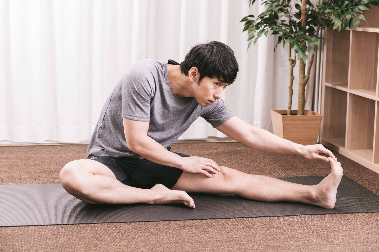 ヨガマットの上で内ももをストレッチする男性［モデル：大川竜弥］