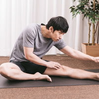 内ももをストレッチする男性がヨガマットで準備運動の写真