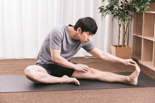 内ももをストレッチする男性がヨガマットで準備運動