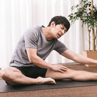 カッチカチやぞ！ヨガマットで前屈ストレッチをする男性の写真