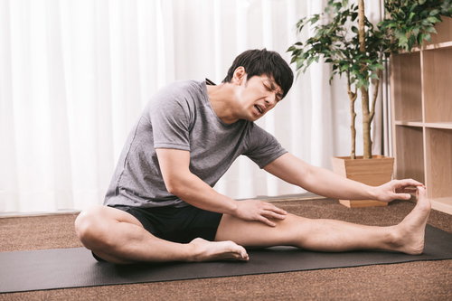 カッチカチやぞ！ヨガマットで前屈ストレッチをする男性