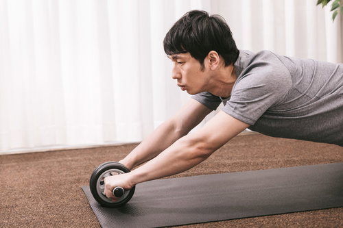 ジムでアブローラーを使って腹筋を鍛えるトレーニング中の男性