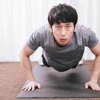 室内でマットの上で腕立て伏せをするトレーニング中の男性の写真