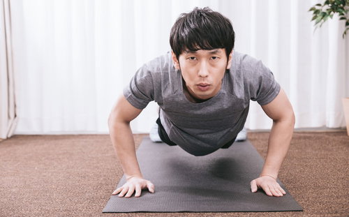 室内でマットの上で腕立て伏せをするトレーニング中の男性