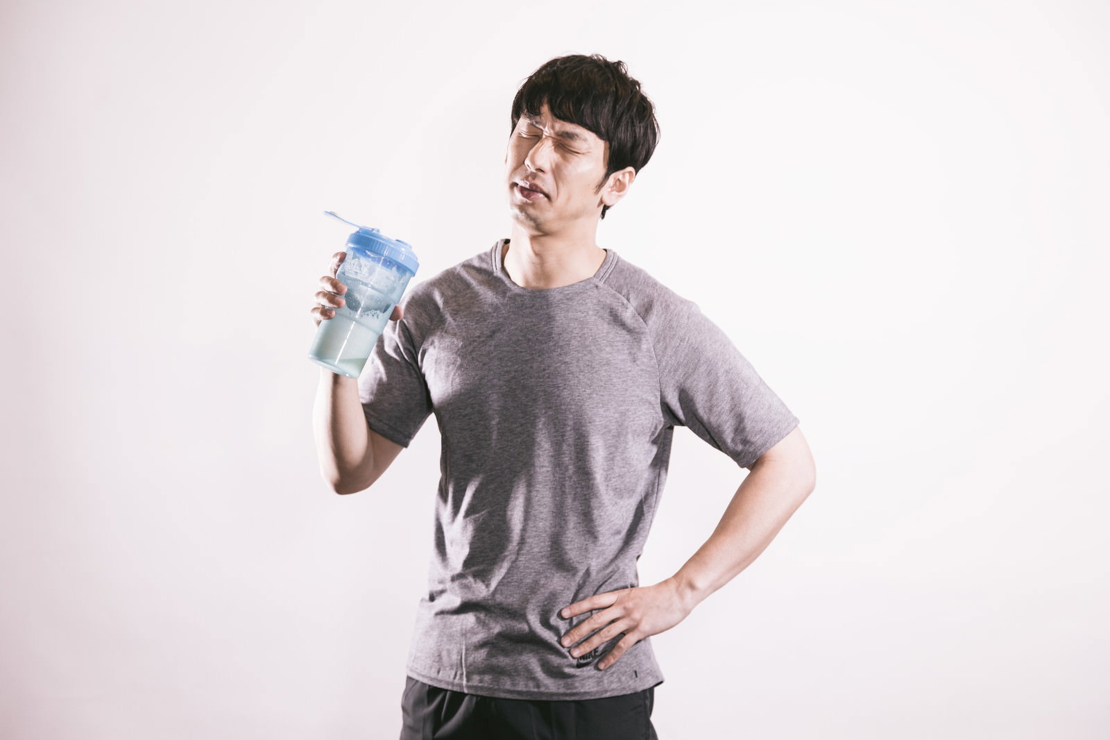 プロテインシェイクを持ちながら困った表情の男性［モデル：大川竜弥］