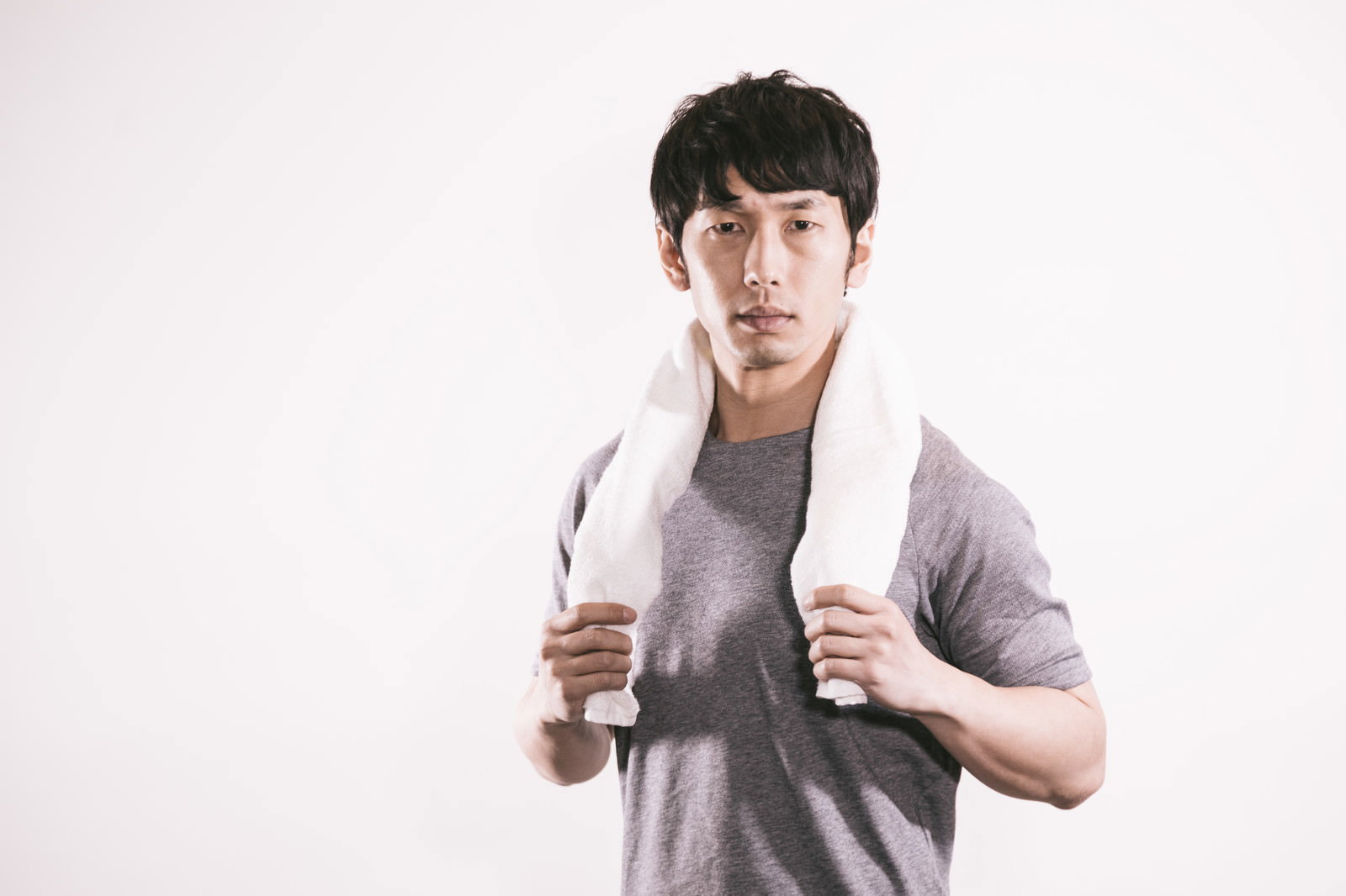 白いタオルを首にかけたグレーのタンクトップの男性トレーナー［モデル：大川竜弥］