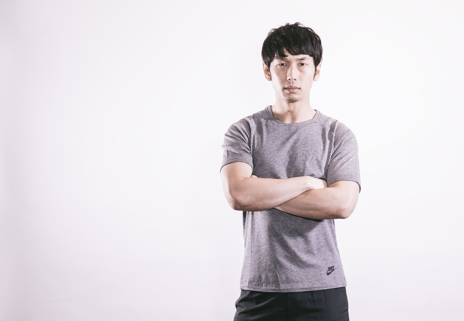 グレーのTシャツを着て腕組みをする真剣な表情の男性［モデル：大川竜弥］