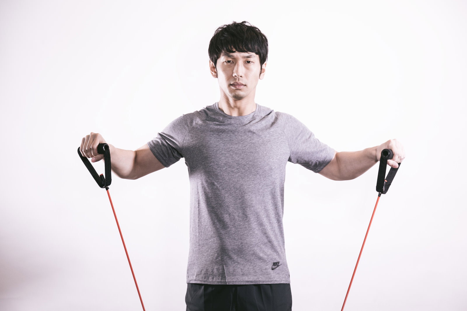 グレーのTシャツを着た男性がトレーニングチューブで肩の筋トレを行う様子［モデル：大川竜弥］