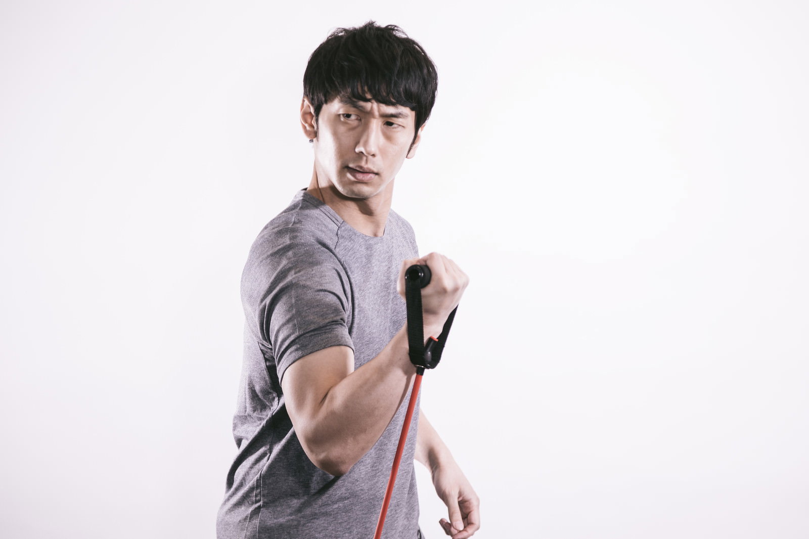 赤いトレーニングチューブを持ち、力こぶを見せるドヤ顔の男性［モデル：大川竜弥］