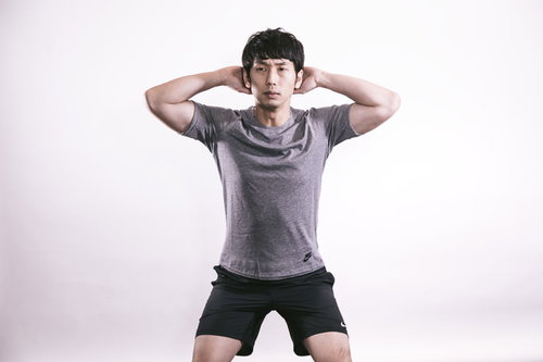 両手を頭の後ろに置いてスクワットをするトレーニー