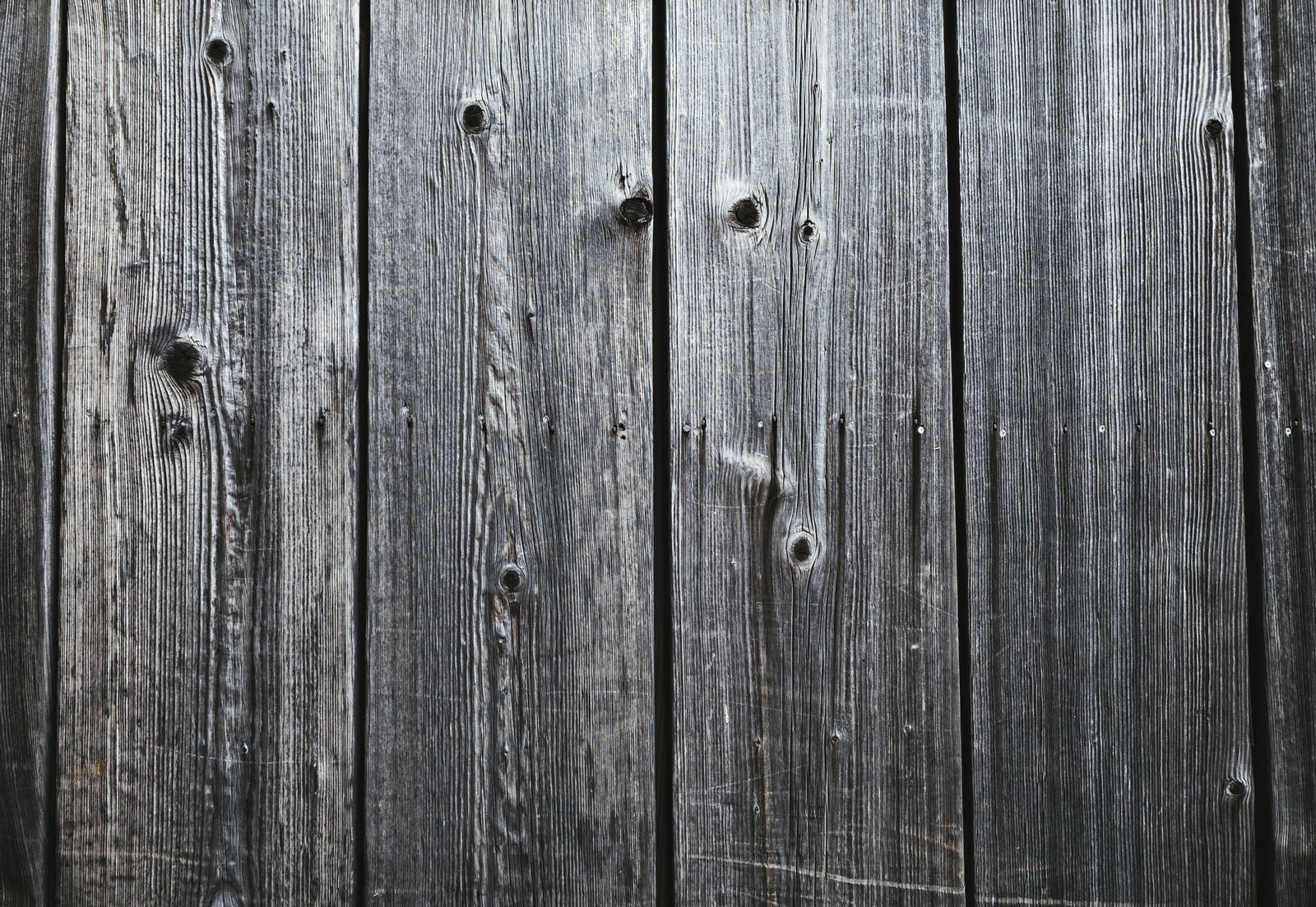 縦並びの古い木製板、灰色に風化した表面に黒い節穴と釘跡が散在