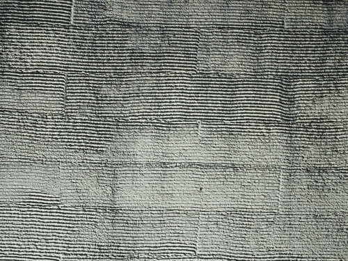 グレーと深緑のモルタル壁に走る規則的な線状凹凸