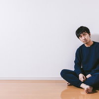 何もない部屋の隅で座り込む男性の写真
