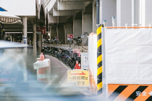 駅前の駐輪場に並ぶ赤やピンク色のシェアサイクルと黒紺の自転車群