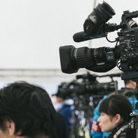 報道陣が集結する取材現場でのテレビカメラとマイク・照明の装備風景の写真