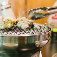 網の上で焼く鶏肉とピンセット型トングを持つ手の写真