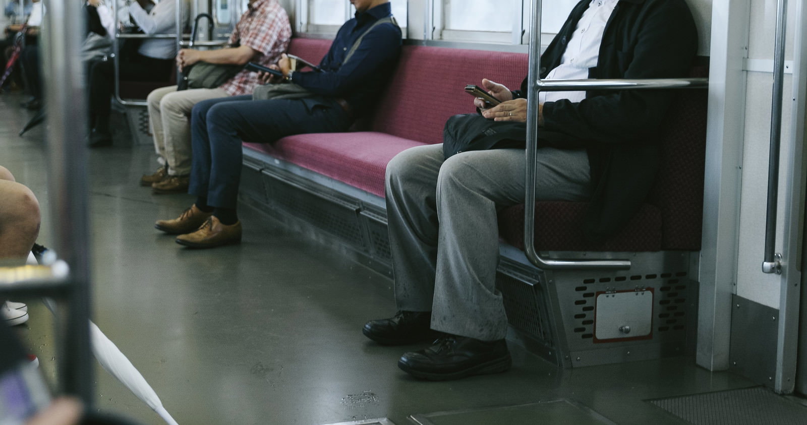 通勤電車の座席に座ってスマートフォンを見ている乗客たち