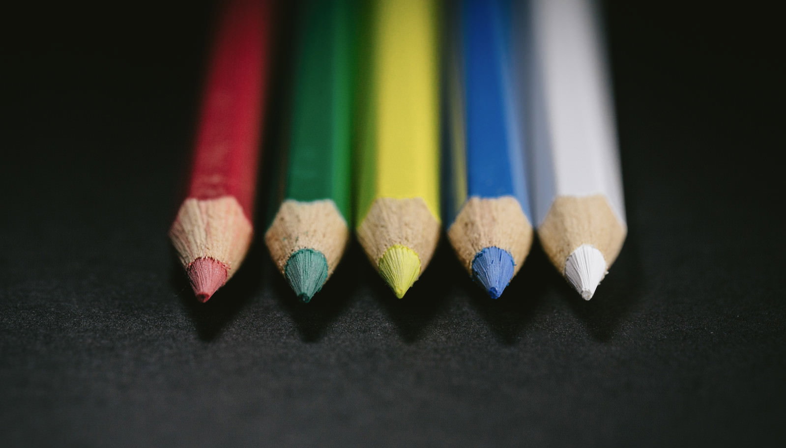 黒い背景に5本の色鉛筆が先端を揃えて並ぶ