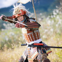 白髪の武将が太刀を構える赤い当世具足と骸骨兜の戦国武士姿の写真