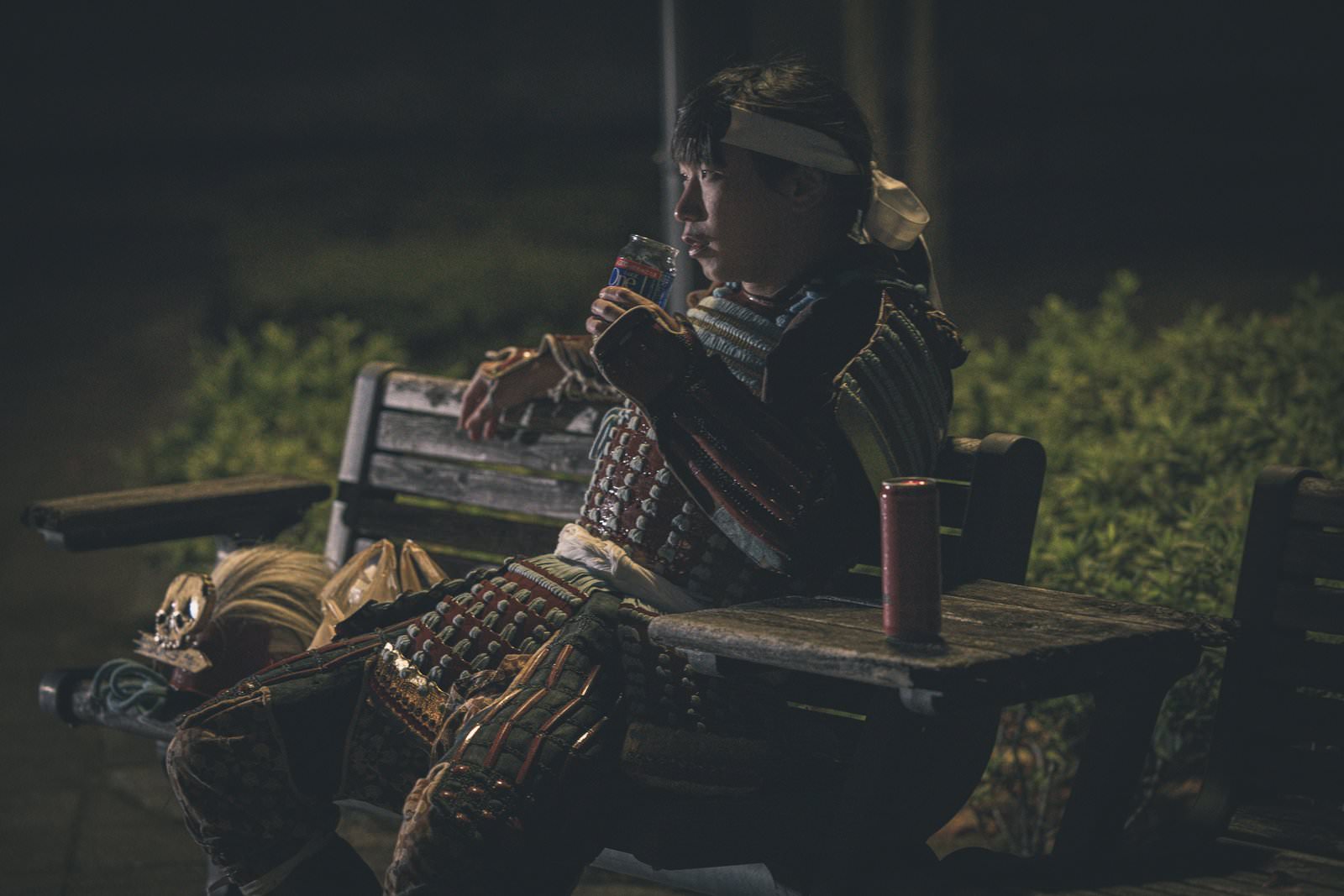 夜の公園のベンチで日本酒を飲んでいる甲冑を着た侍の男性［モデル：まーこ］