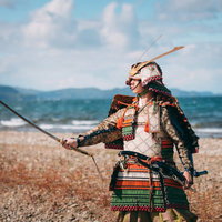 猪苗代湖岸で日本刀を翳す当世具足姿の侍が力強く立つの写真