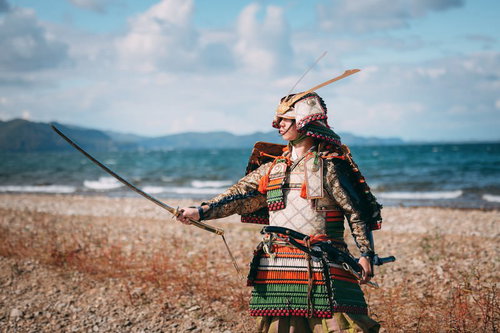 猪苗代湖岸で日本刀を翳す当世具足姿の侍が力強く立つ