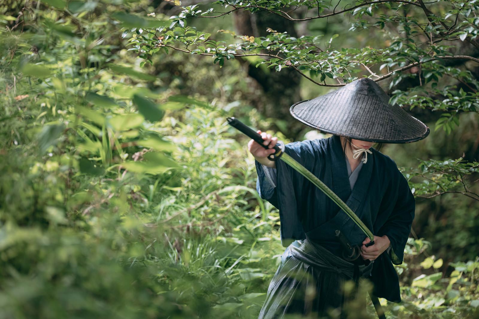 緑の藪に隠れて太刀を鞘に収める網代笠を被った侍［モデル：まーこ］