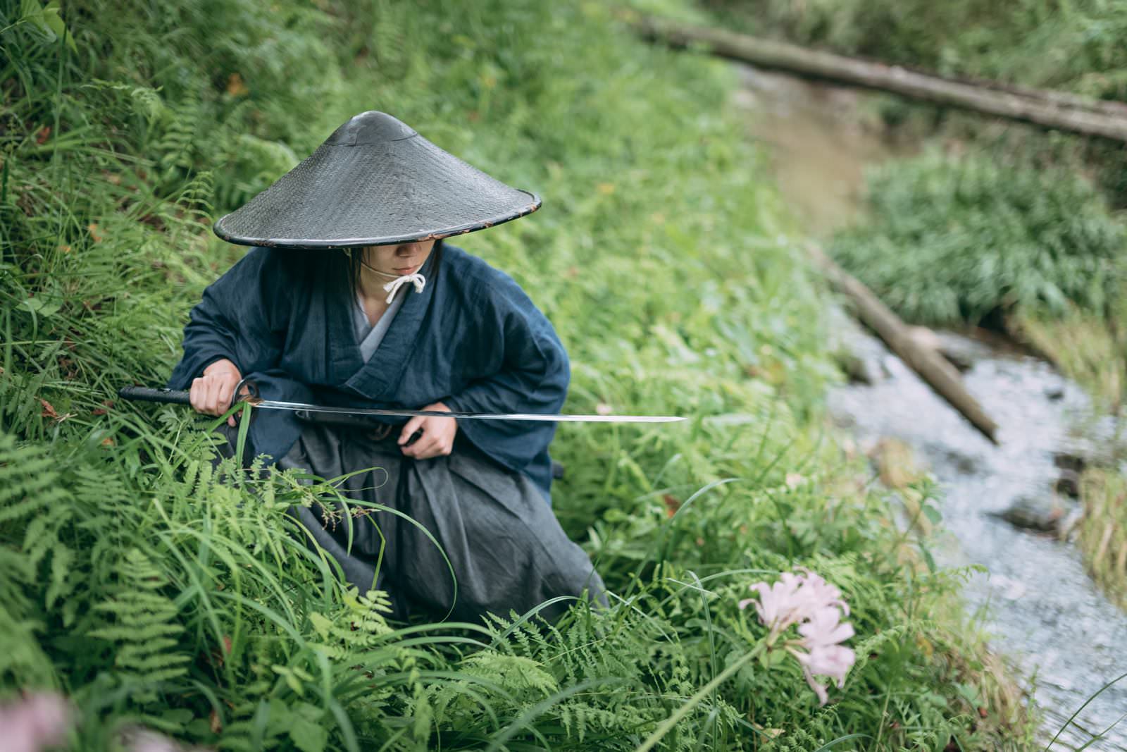 網代笠を被り袴を着た侍が水辺で刀を構えている様子［モデル：まーこ］