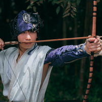 紫の鉢巻きで弓を引く野盗、集中した表情で弓矢を構える和装の男性の写真